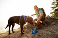 Man pouring water into a collapsible dog bowl for travel while hiking with his dog.