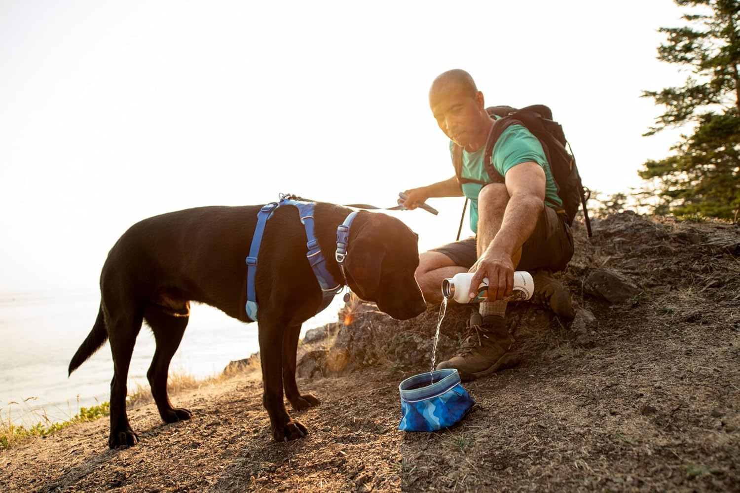 Man pouring water into a collapsible dog bowl for travel while hiking with his dog.